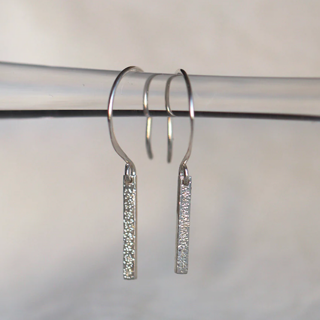 Silver hoop earrings with diamond-studded bar pendants on a white background