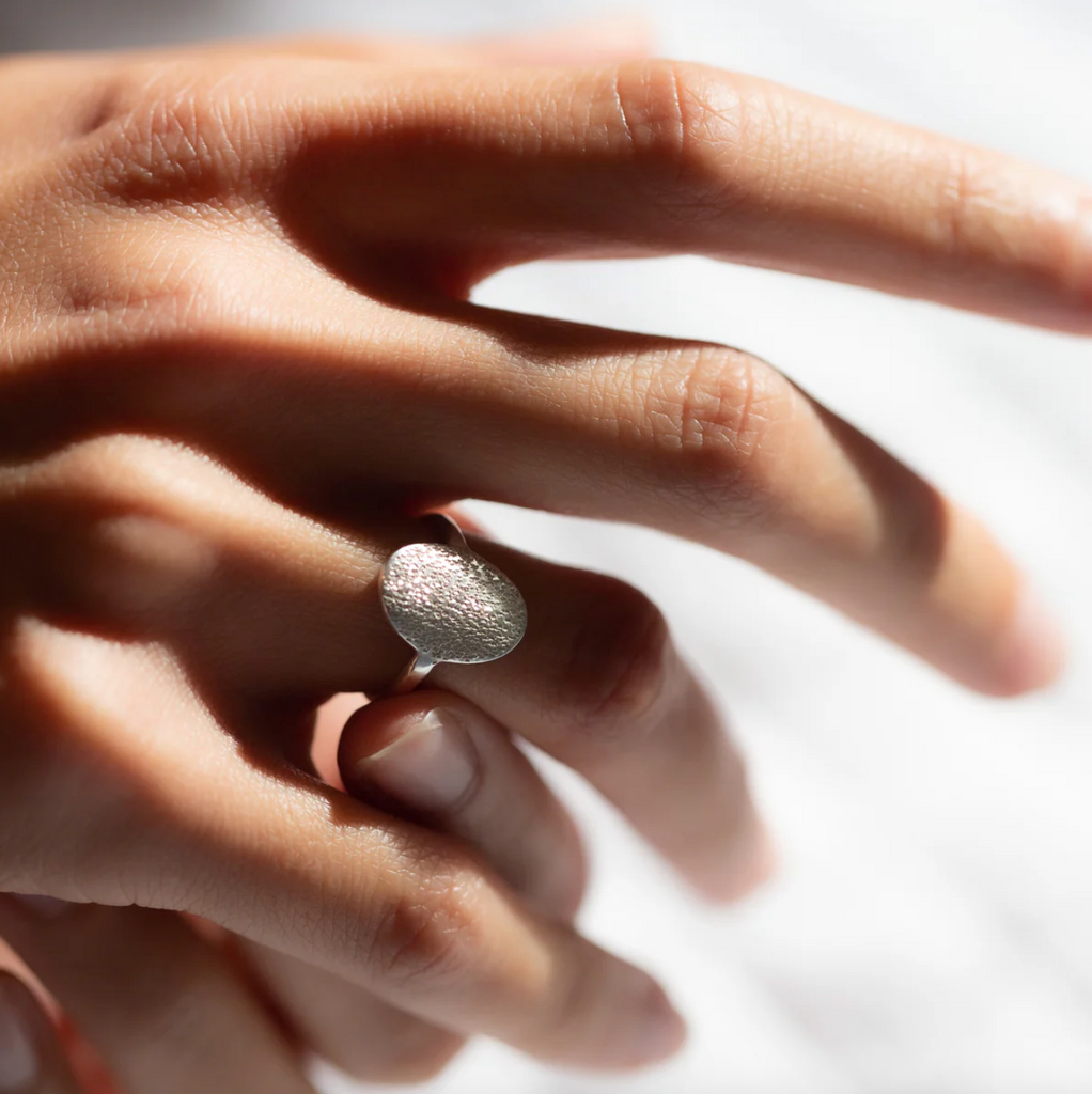 Hand wearing a textured silver ring on a light background