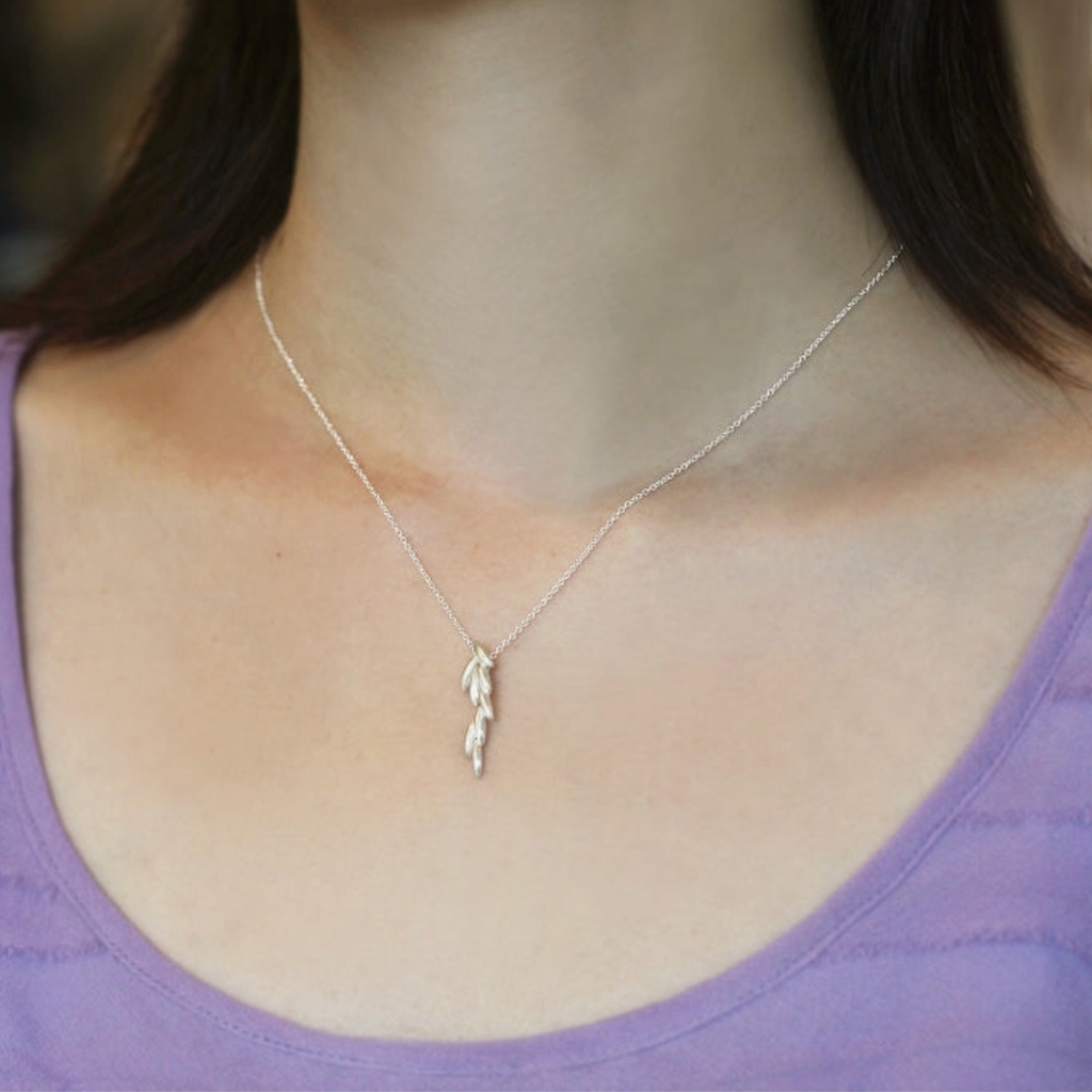 Silver necklace with a leaf pendant worn by a person in a purple top.
